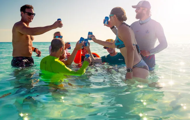 Group of people stood in clear water and celebrating with a canned drink