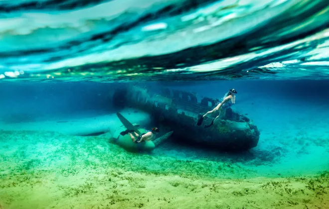 Man and woman snorkelling next to a plane wreck in clear water