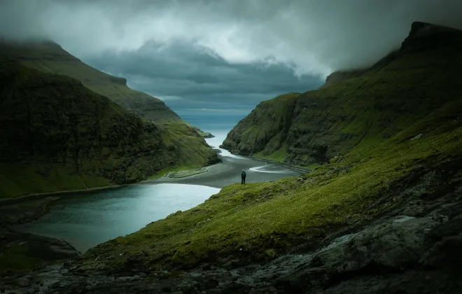Participant stood on rocky and green terrain, looking out to dark water