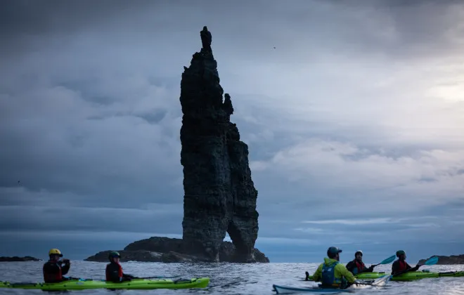 Participants kayaking past large rock