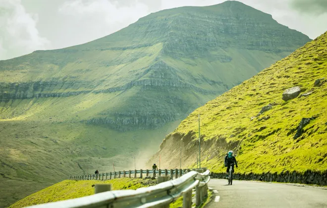Cyclist riding along road with green mountain in the background