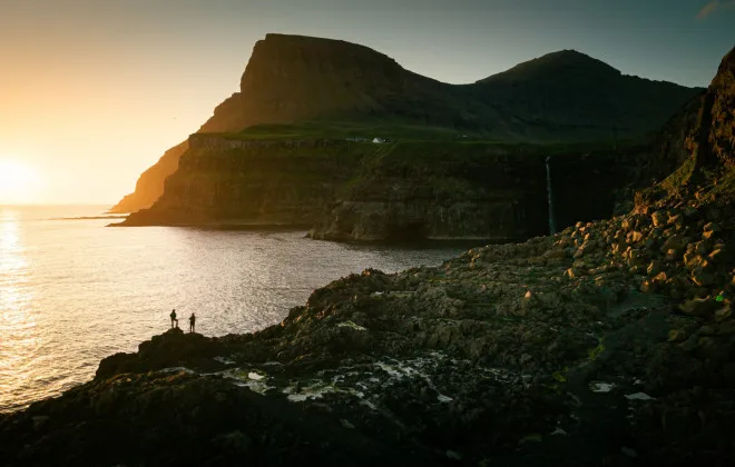 Participants stood on rocky terrain, looking out to sea at sunset