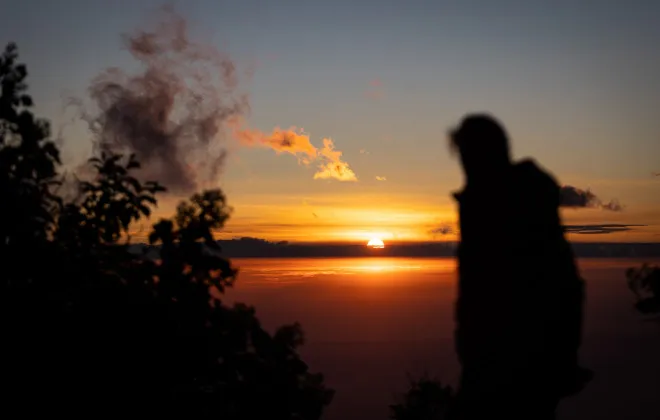Silhouette of person looking out to sun setting