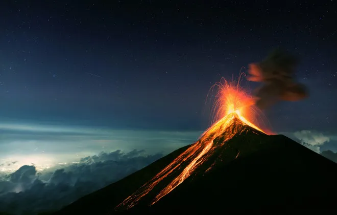 Volcano erupting with bright lava as a still, starry sky lies above