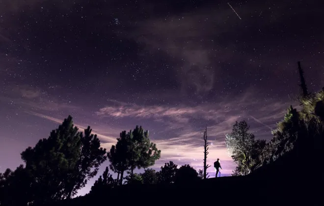 Person hiking with a dark, starry sky above