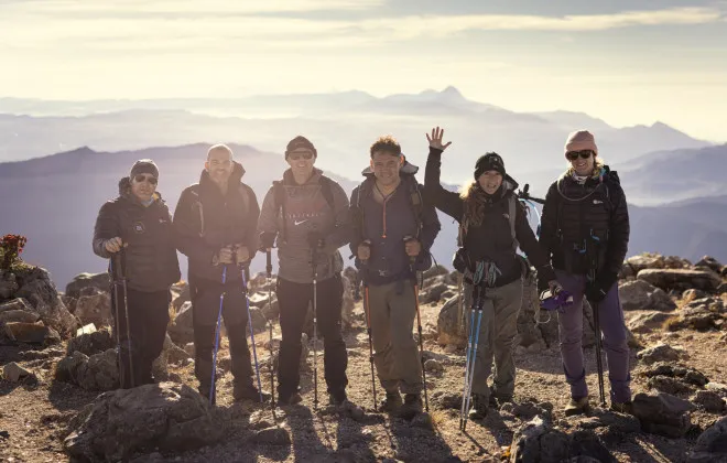 Six people stand on rocky terrain with mountains in the background