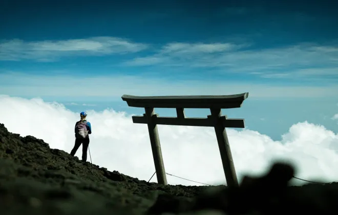 Woman stood on rocky terrain, looking out to bright sky and clouds