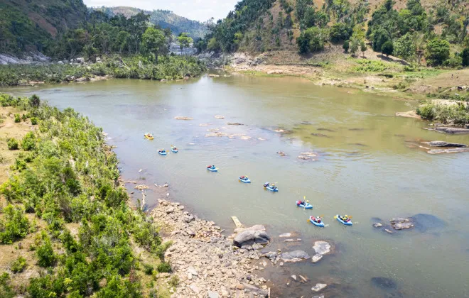 Participants rafting in water surrounded by rocky terrain, sparse trees and mountains