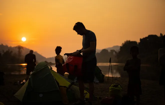 Participants unpacking their tents as a colourful sun sets in the background