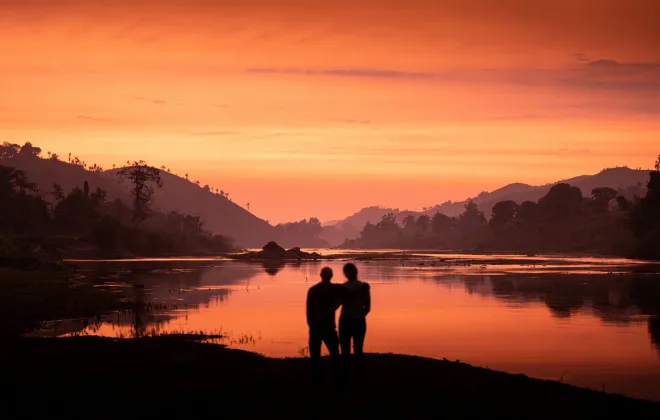 Silhouettes of two participants with their arms around one another with colourful sky above