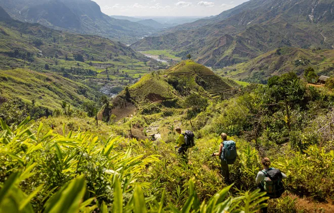 Group of participants trekking through tropical grassland with mountains in the background