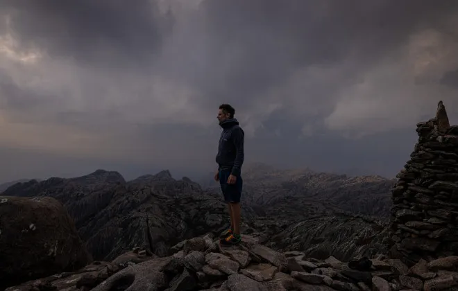 Man stood on rocks with grey sky behind him