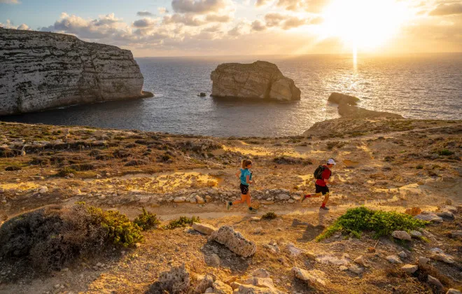 Man and woman running along rocky coastline