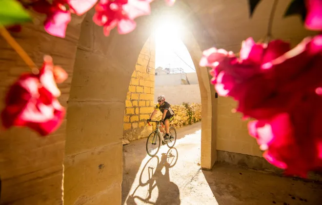Cyclist rides past archway, leading to colourful flowers
