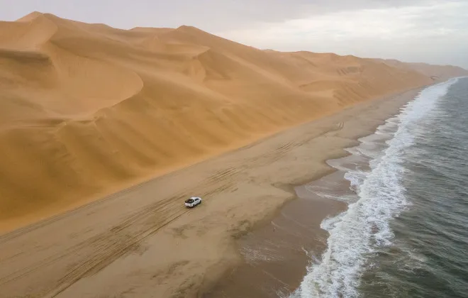 Car travelling along sandy coastline, between sea and sand dunes