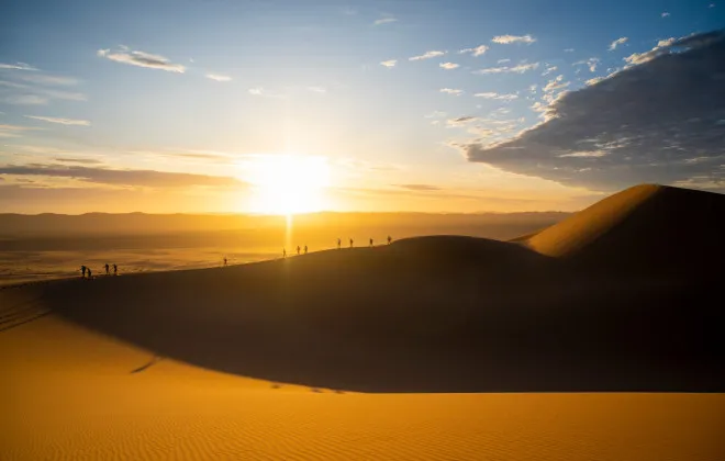 Participants walking over sand dunes with low sun beside them