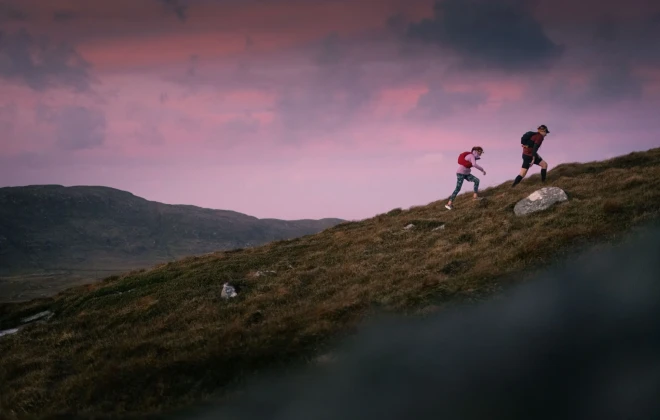 People walking up grassy hill with colourful sky behind