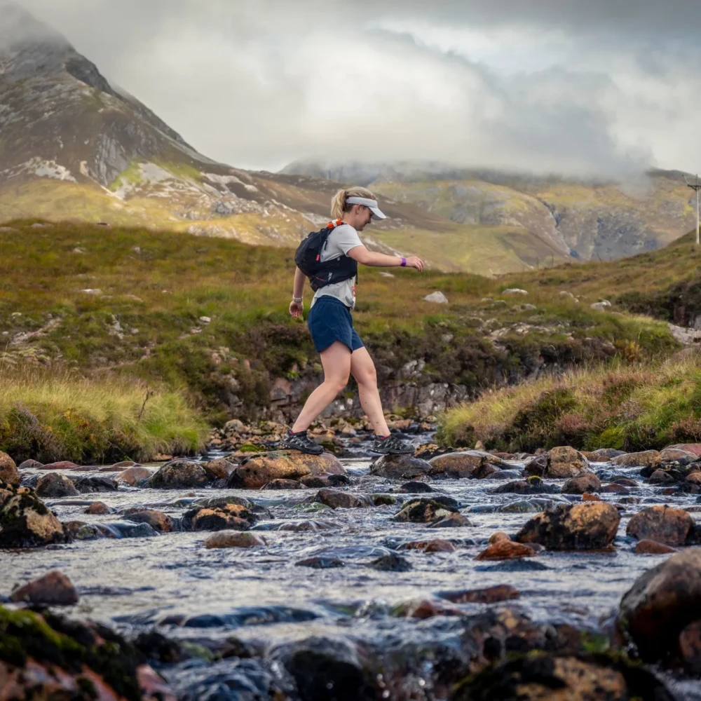 Woman crossing stream, surrounded by greenery