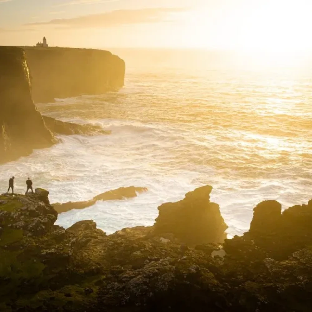 People stood on cliff edge, looking out at sea and sun