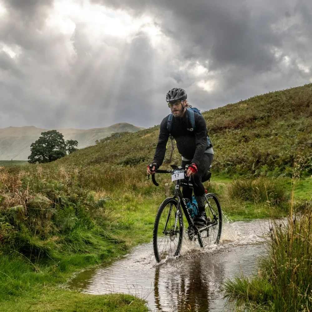 Man cycling through water with greenery either side of him