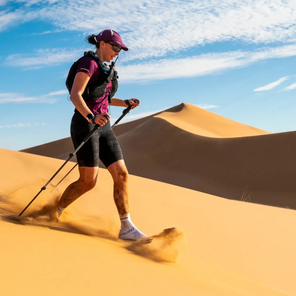 Woman running down sand dune using trekking poles