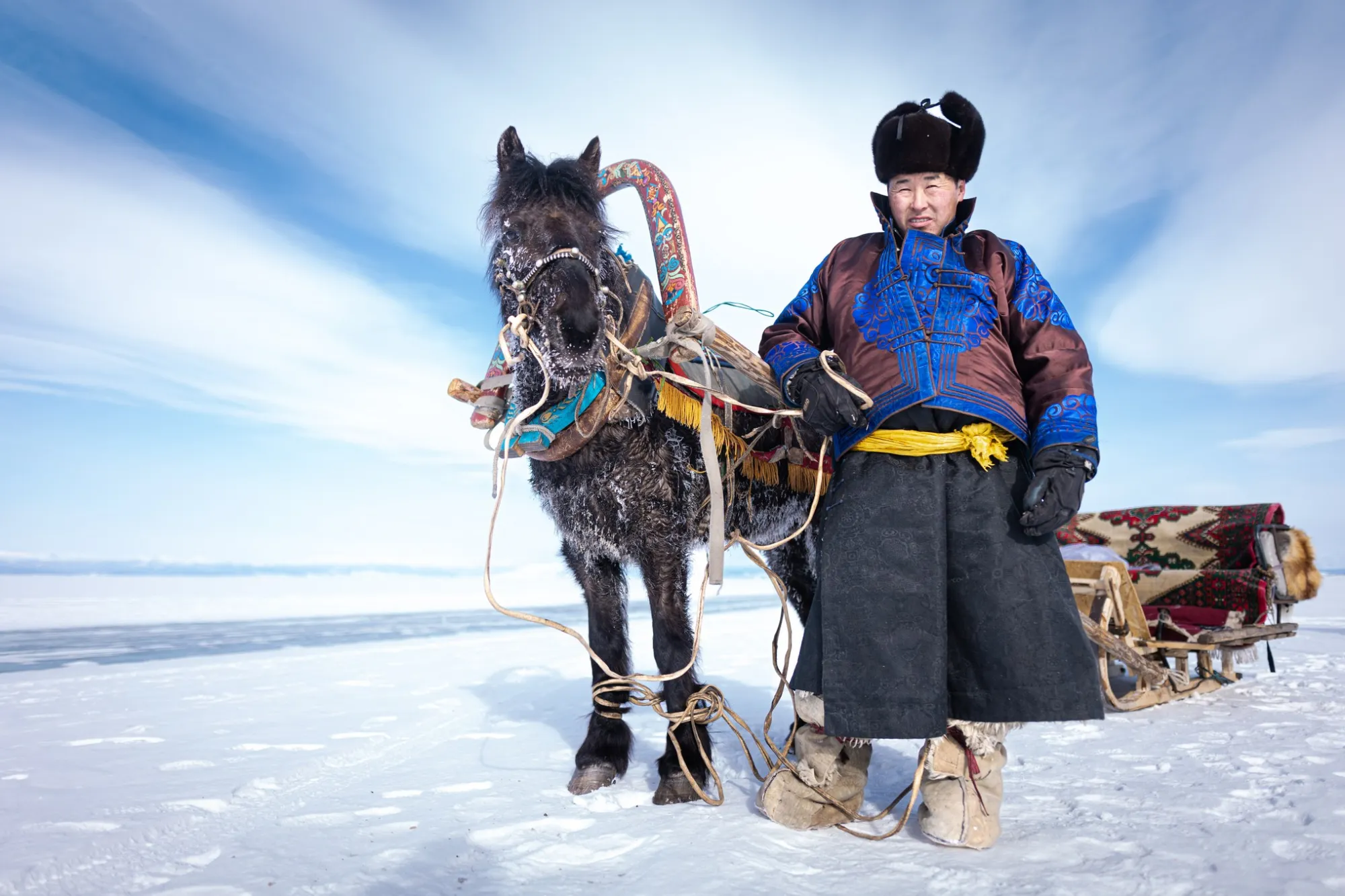Man stood on snow with a horse and sled